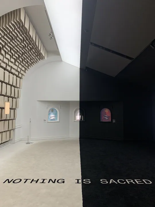 NOTHING IS SACRED 문구가 있는 흰 전시 공간